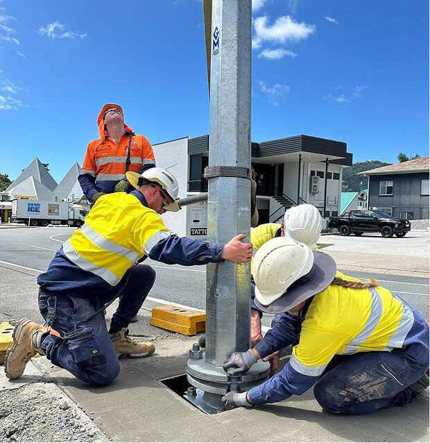 Road services crew installing a traffic signal pole, with technicians securing the base and fittings to ensure safe roadside infrastructure.